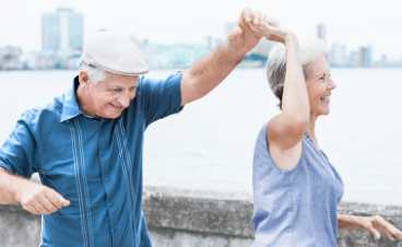 Oudere man en vrouw dansen en hebben plezier buiten in de buurt van water/ zee met een stad op de achtergrond.